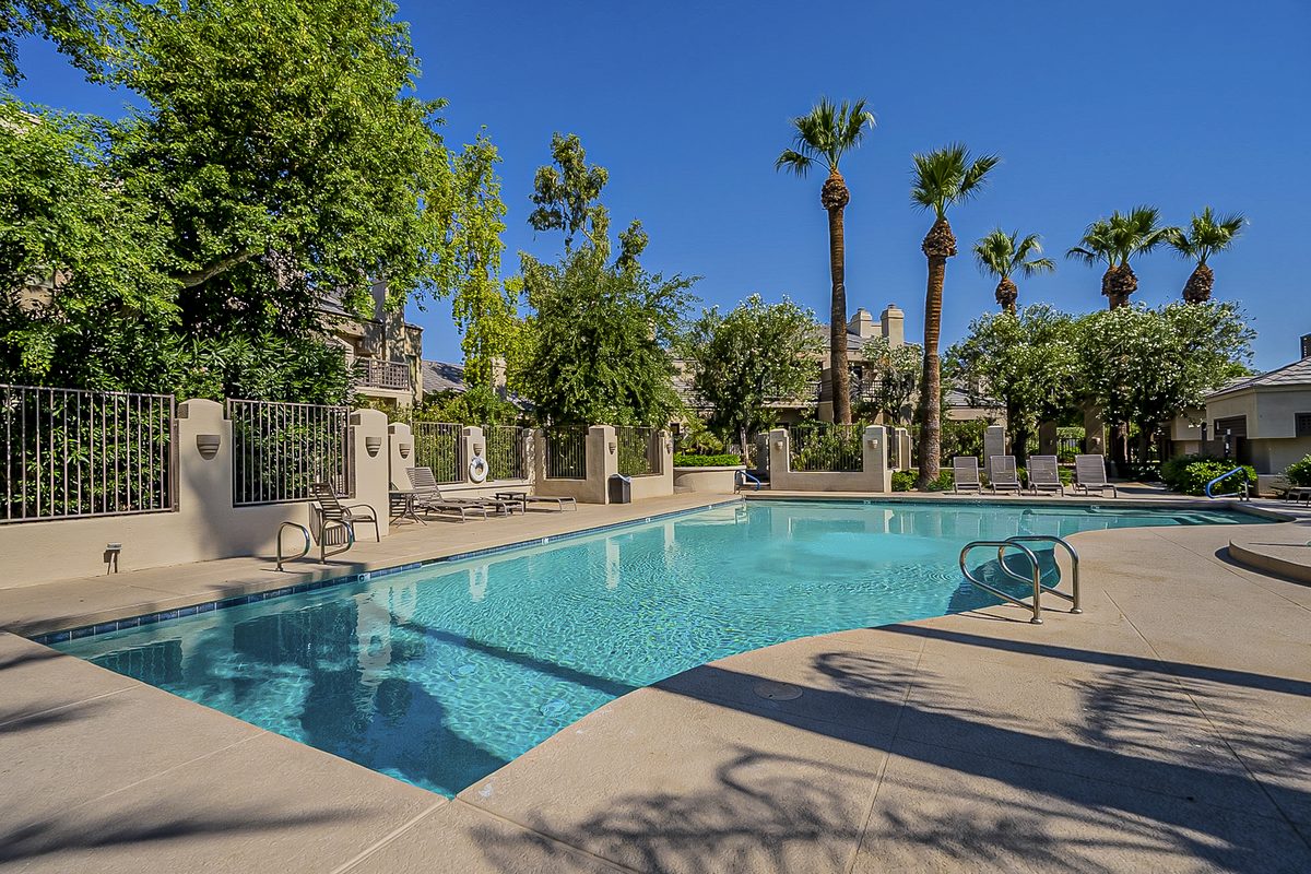 Residential community swimming pool with lounge chairs, wrought-iron fencing and tall palm trees in Gainey Ranch, Scottsdale