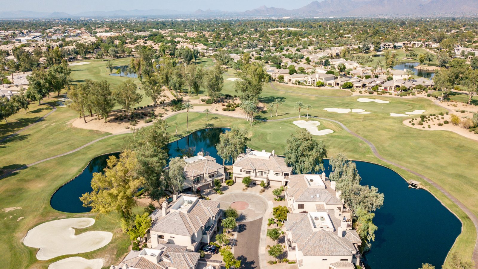 Aerial view of Gainey Ranch homes beside a lagoon and golf course fairway with the McDowell Mountains in the distance, Scottsdale